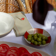 Table setting with sliced tomatoes, green grapes, and a napkin with a red flower on a textured surface.