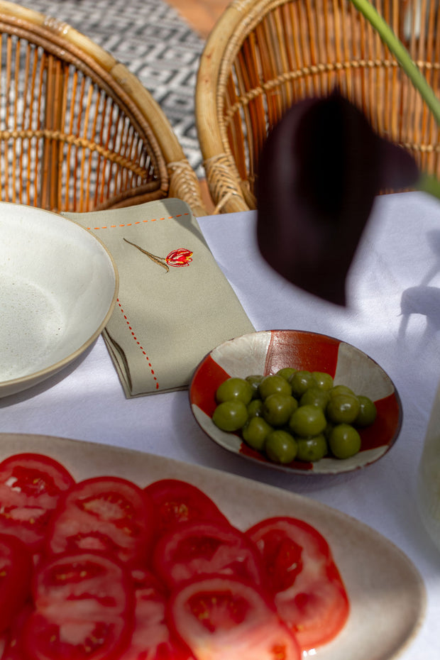Table setting with sliced tomatoes, green grapes, and a napkin with a red flower on a textured surface.
